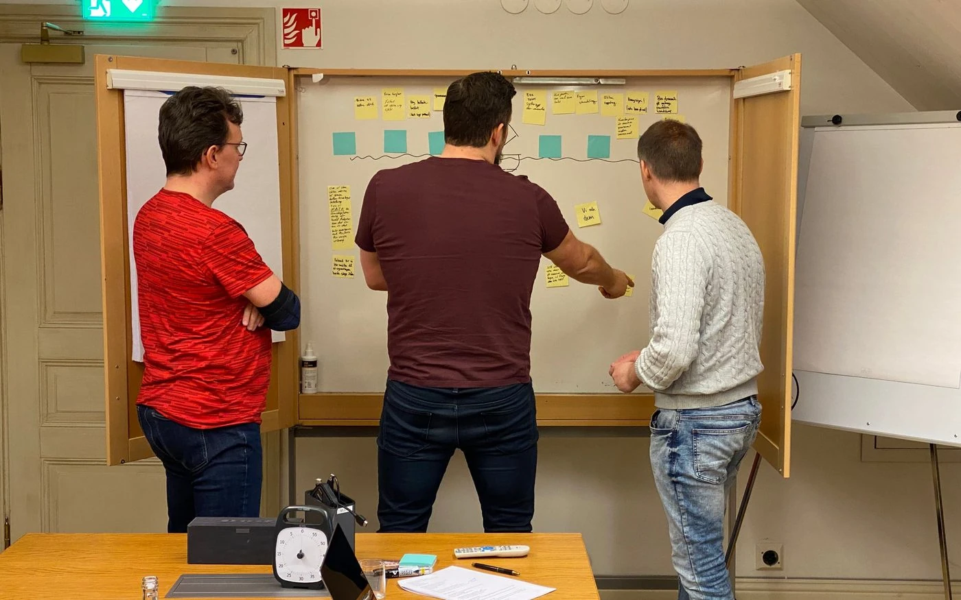 Tre män framför en whiteboard med gula lappar, en pekar och diskuterar