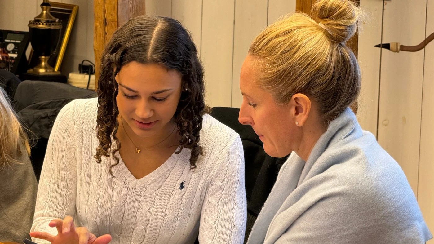 Två kvinnor sitter tätt intill varandra och tittar ner på en mobiltelefon
